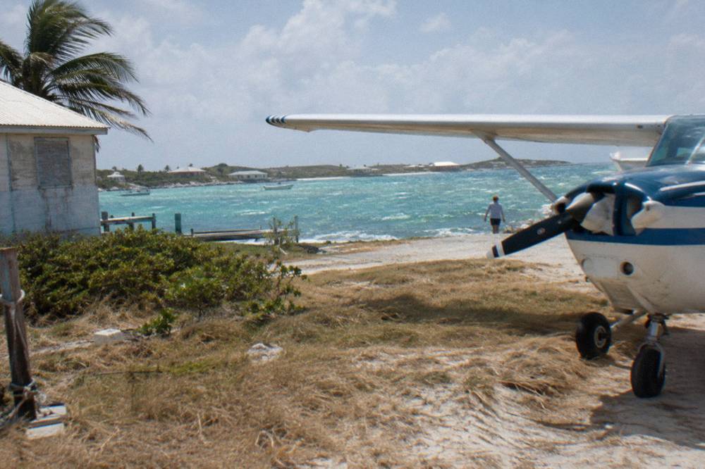 A small plane parked on a grass airstrip beside a turquoise bay