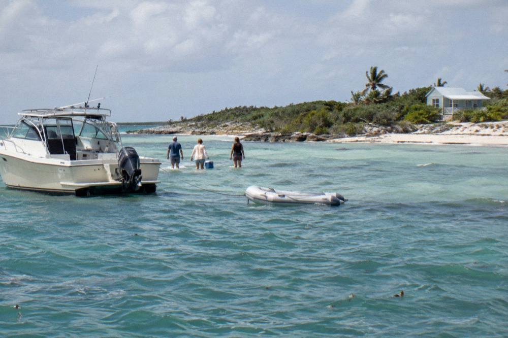 Private boat anchored off a small cay with guests wading ashore