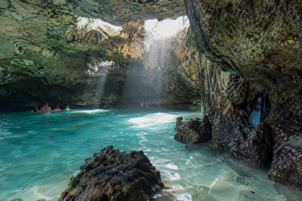 Sunbeams shining through holes in a cave ceiling onto clear turquoise water
