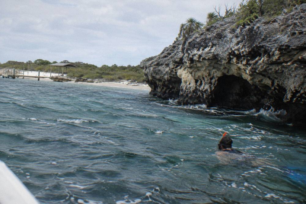 A snorkeler floating in calm turquoise water beside a rocky cay shoreline