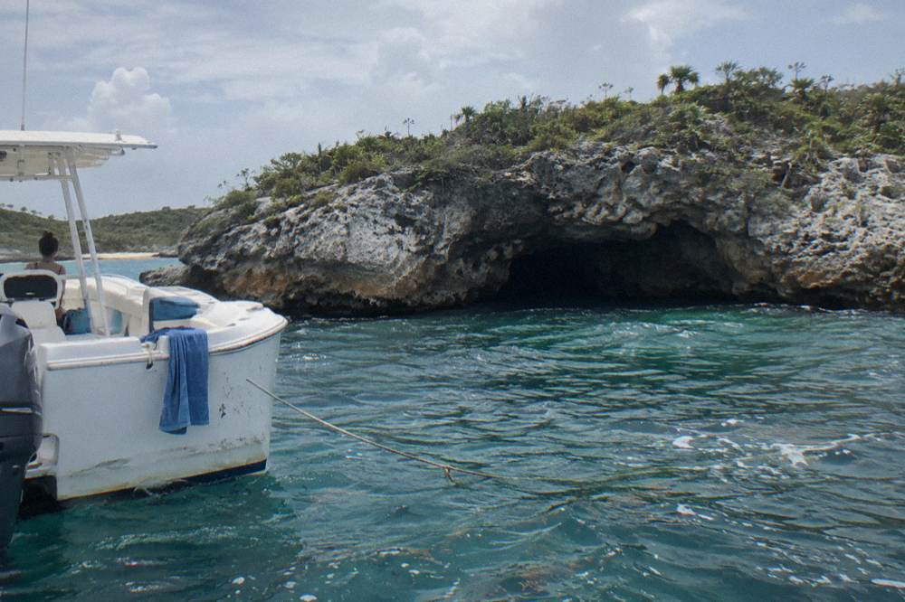 A white powerboat anchored beside a rocky cay with a dark cave opening at the waterline