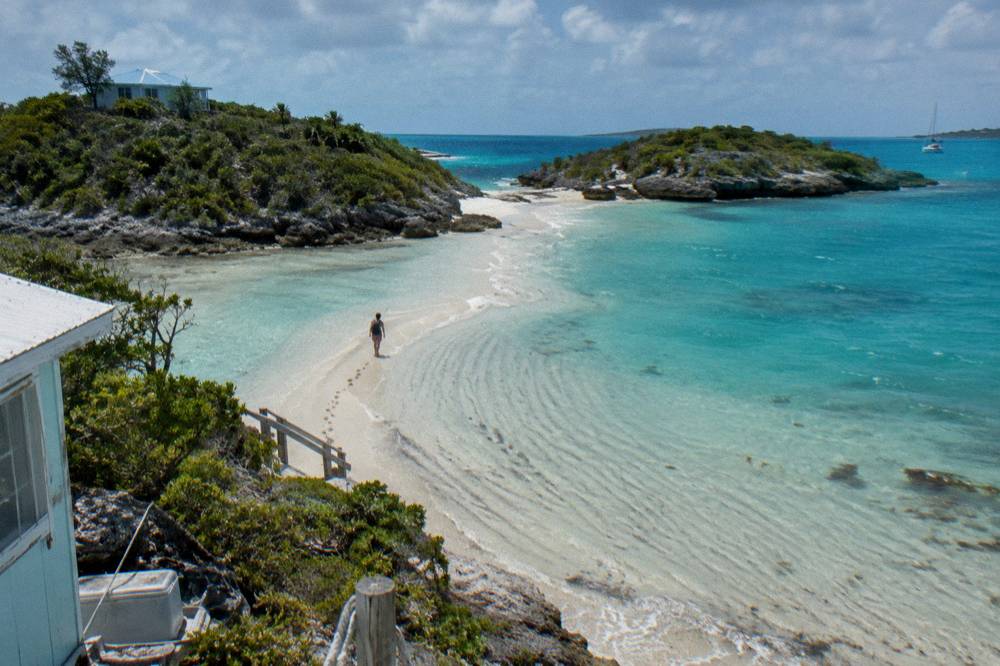 A shallow sandbar curving into clear water between two small cays at midday
