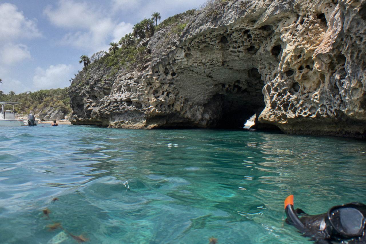 A limestone cave opening reflected in clear turquoise water at a small cay in the Exumas