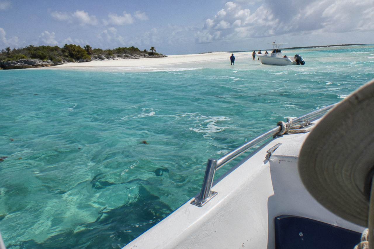 A speedboat anchored beside a white sandbar in clear turquoise water in the Exuma Cays